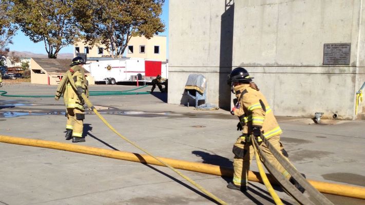 Two trainees pulling a firehose across the training grounds