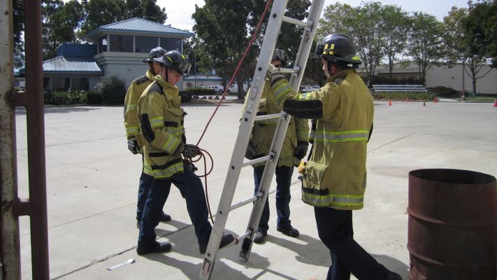 a group of fire personnel around an upright ladder